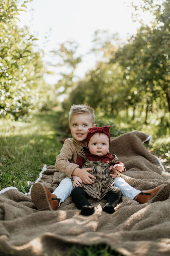 Brother and sister posing for photos in an apple field