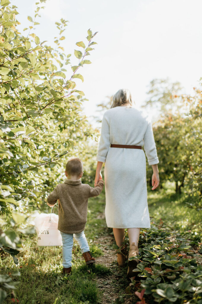 Mother holding her sons hand as they walking through an apple orchard