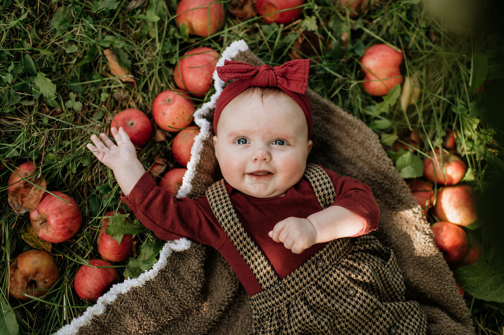 Baby girl laying in the grass of an apple orchard for photos
