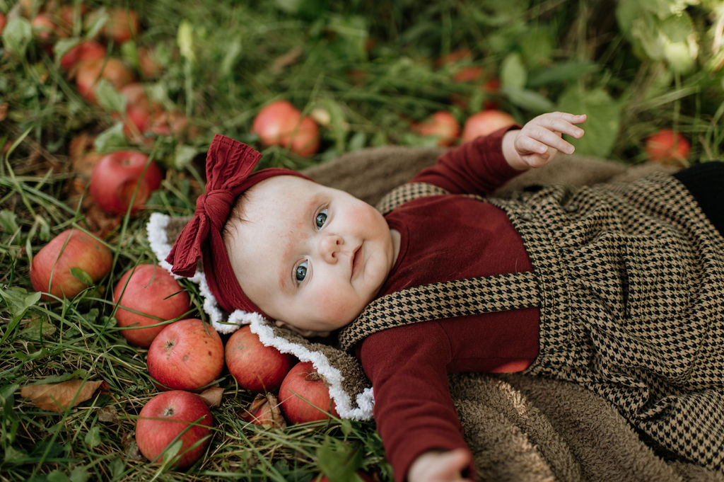 Baby girl laying in the grass of an apple orchard for photos