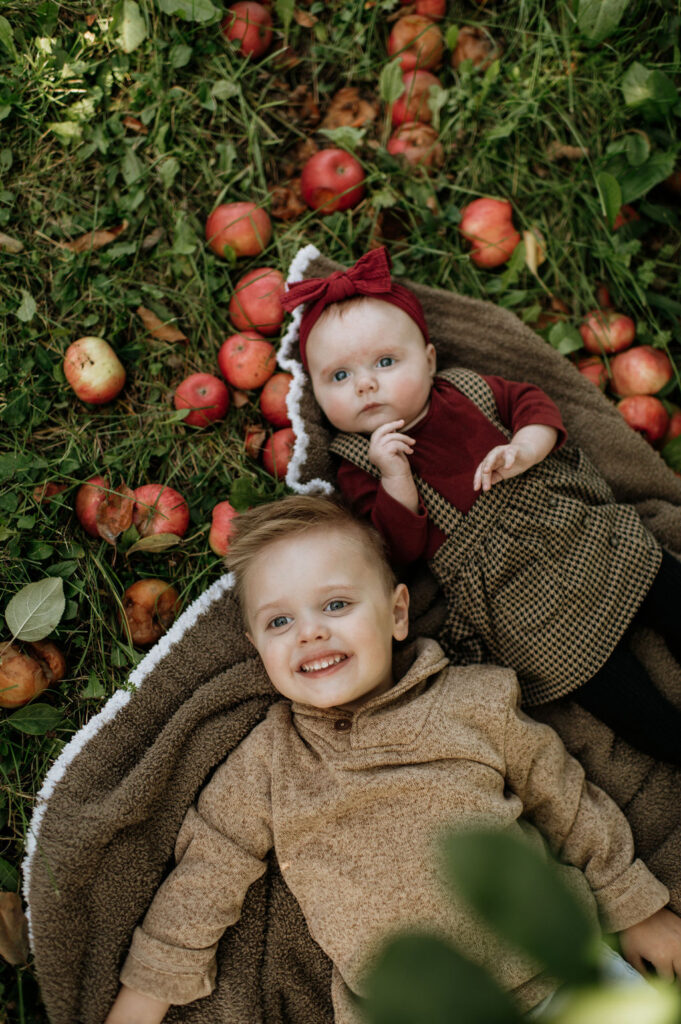 Baby girl and toddler boy laying in the grass of an apple orchard for photos