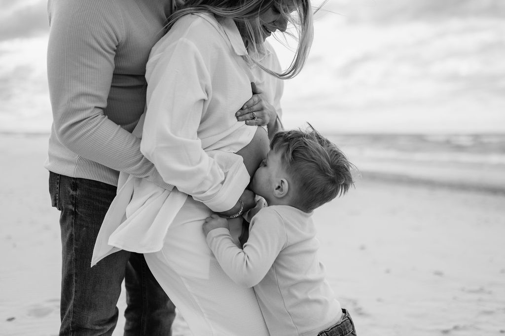 Little boy kissing his mothers pregnant belly at Indiana Dunes National Park for their family maternity photoshoot