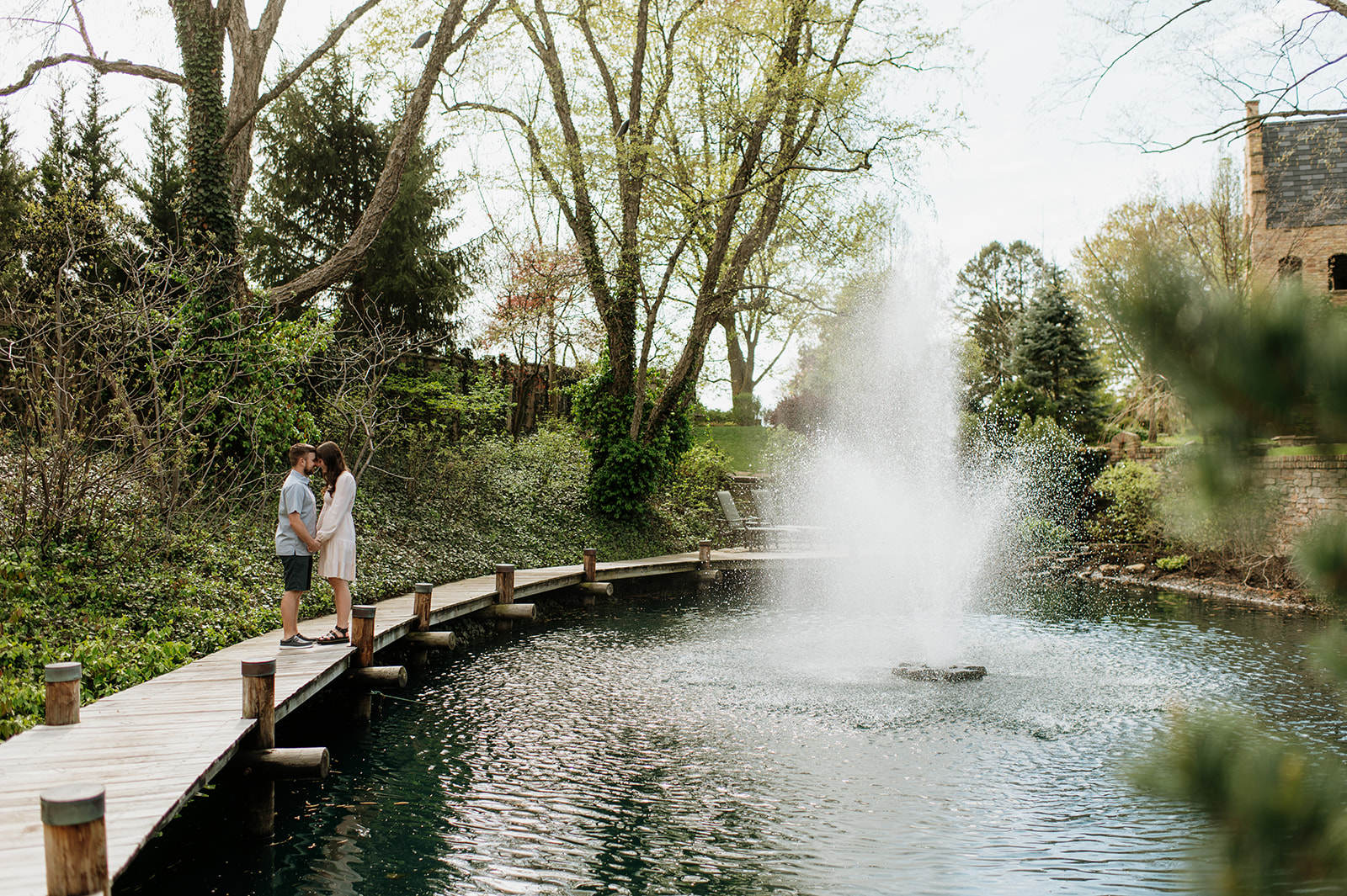 Couple posing for photos by a pond with a water fountain in the middle