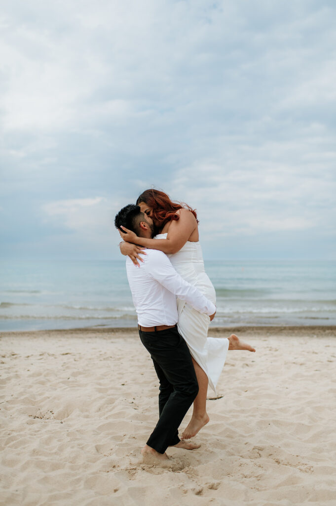 Groom lifting his bride up for a kiss on the beach