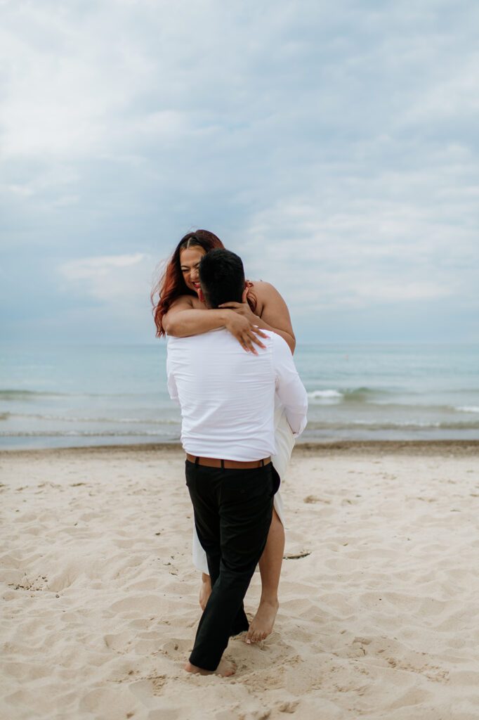 Bride laughing as groom lifts her up on the beach