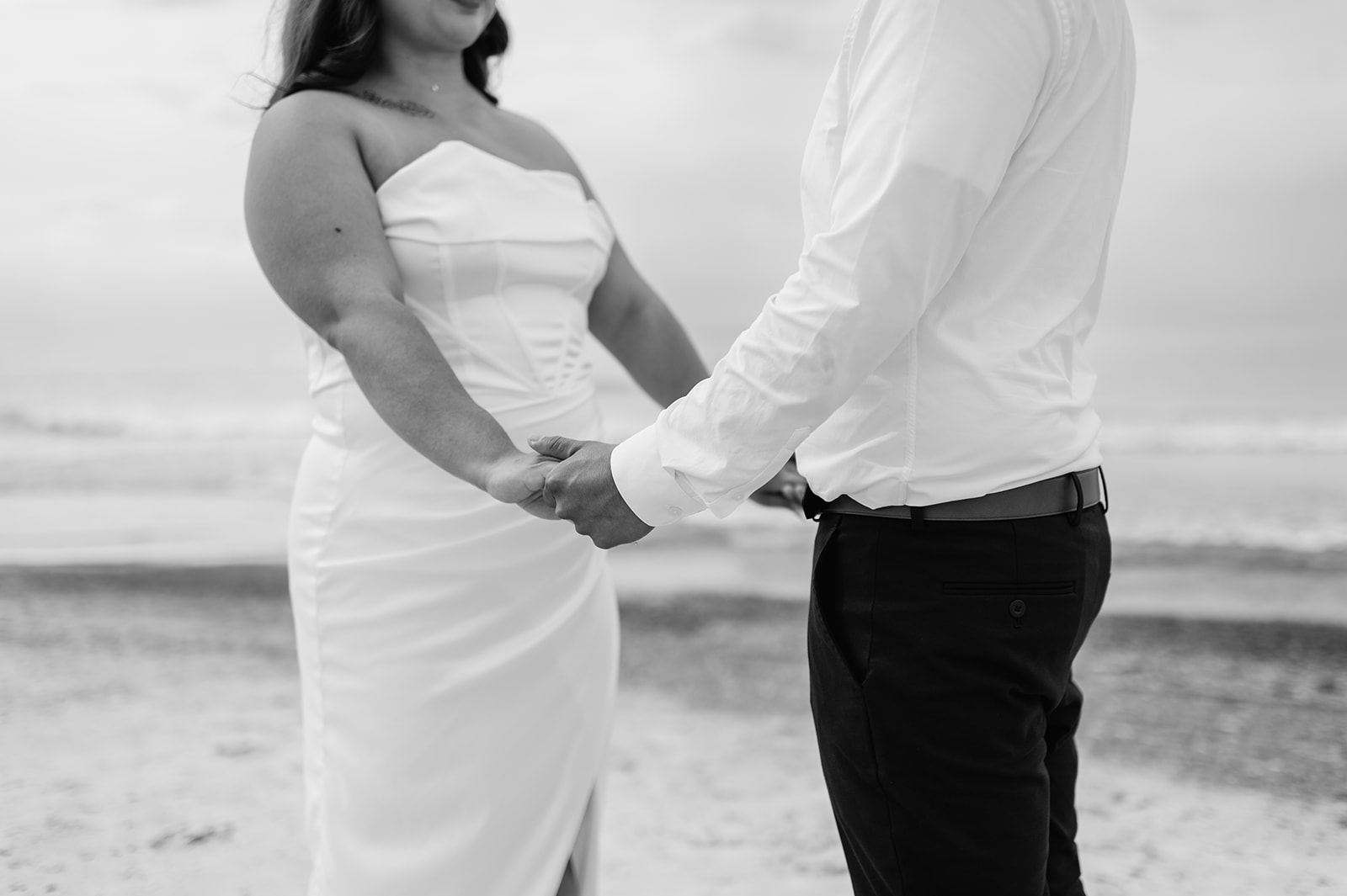 Black and white photo of a bride and groom holding hands during their ceremony