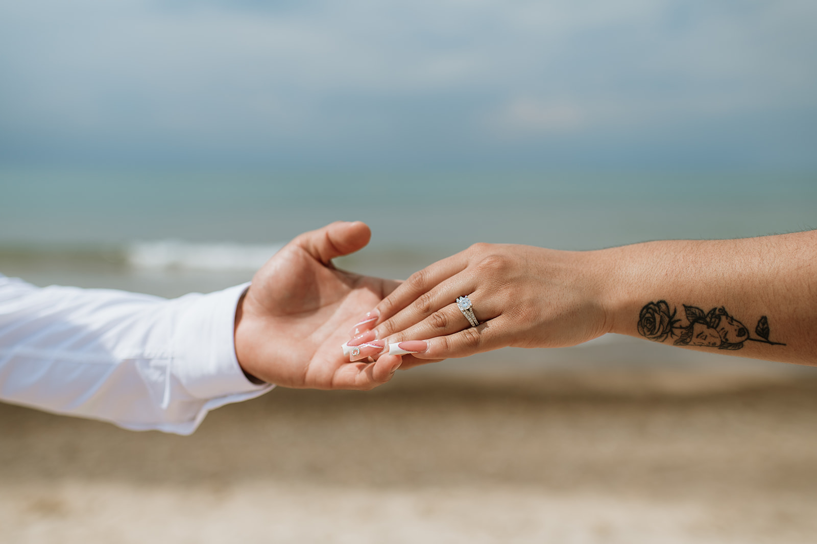 Bride and groom holding hands and showing off their wedding rings on the beach