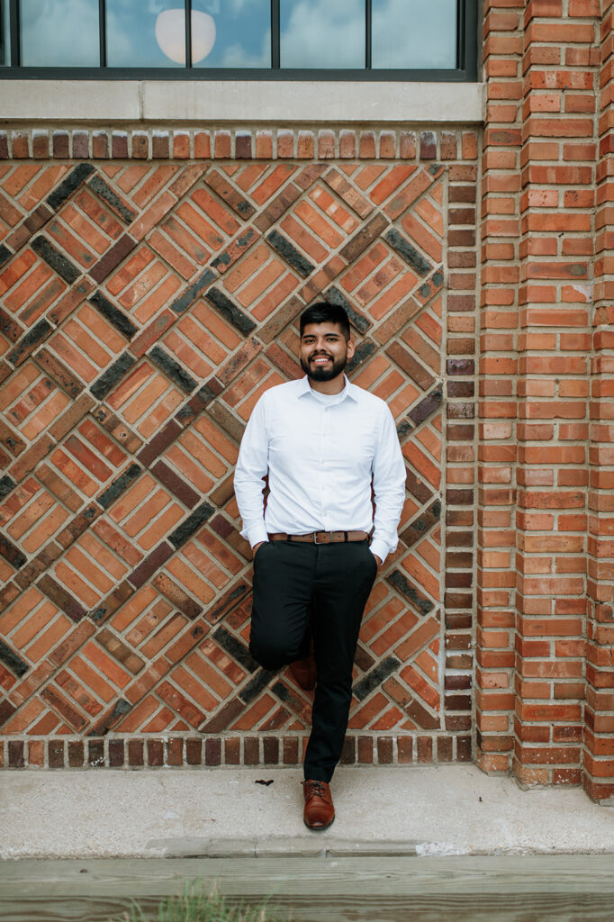 Groom leaning against a brick wall