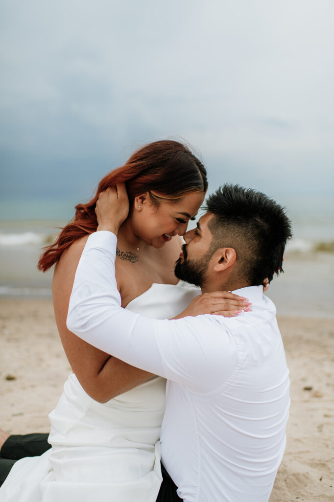 Bride straddling her groom on the beach during their intimate summer elopement