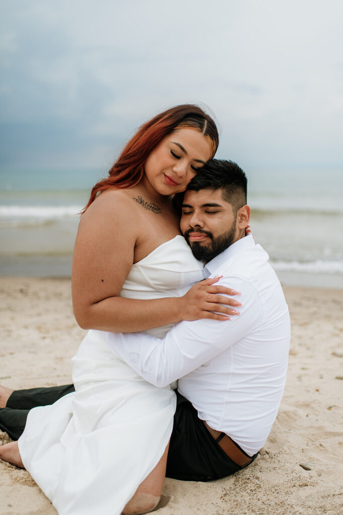 Bride straddling her groom on the beach during their intimate summer elopement