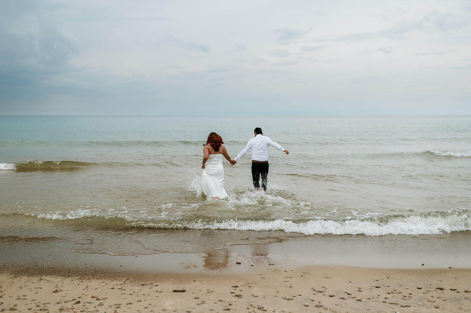 Bride and groom running into Lake Michigan