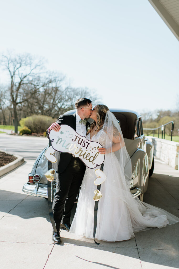 Bride and groom kissing with a just married sign behind a 1940s original Studebaker car