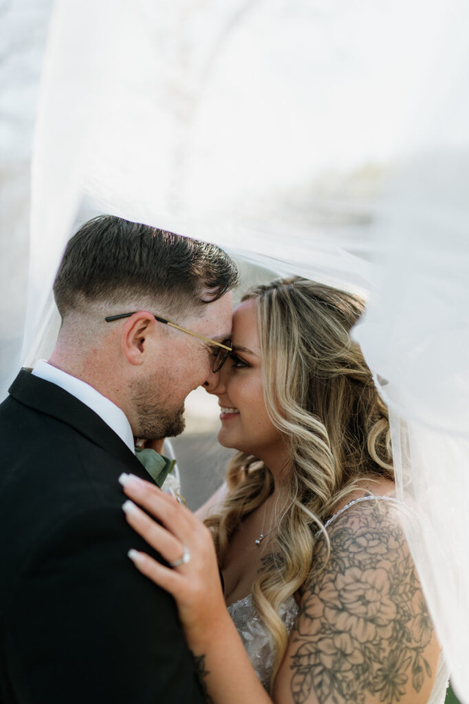 Bride and groom smiling at each other under the brides wedding veil 