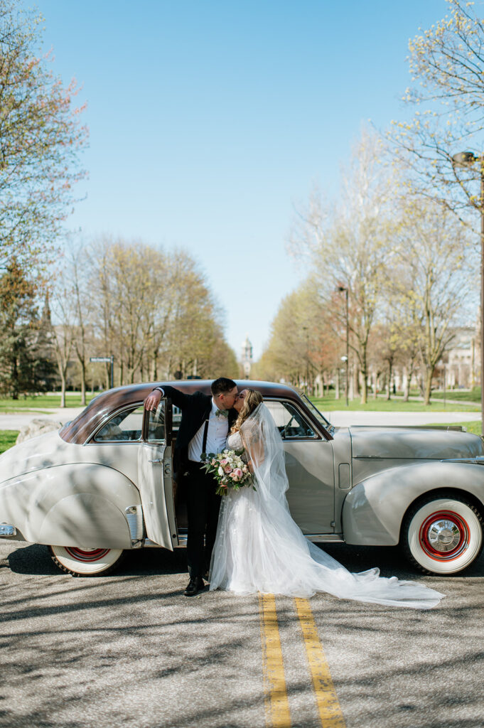 Bride and groom kissing in front of a 1940s original Studebaker car