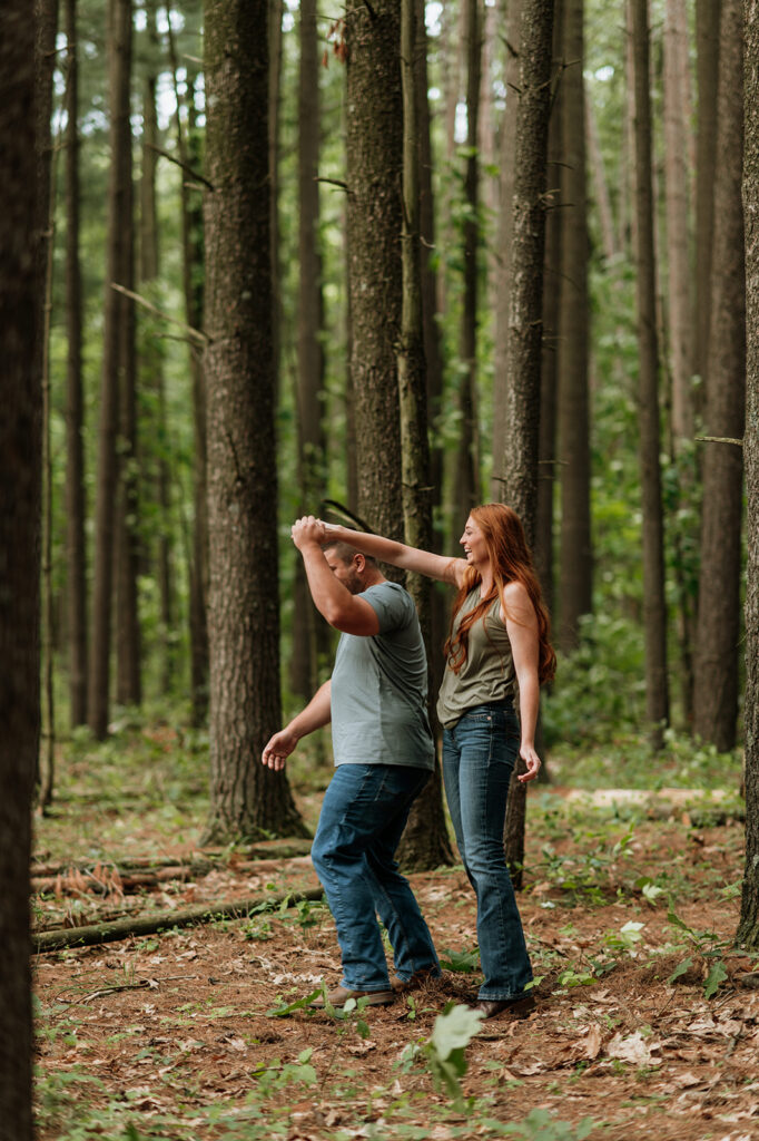 Woman twirling man around playfully during their engagement session in the woods