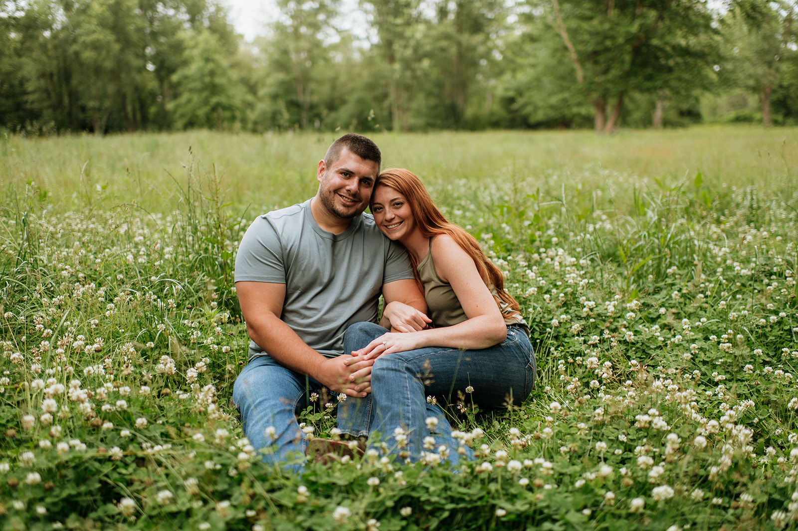 Couple smiling as they sit in a field of wildflowers for their engagement photos in Indiana