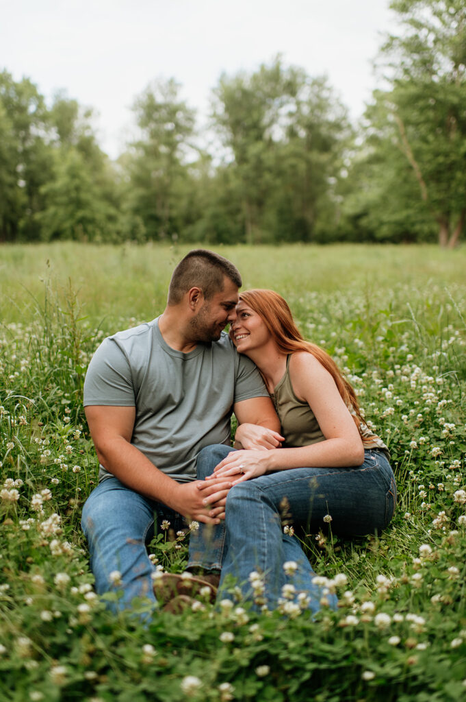 Couple smiling at each other as they sit in a field of wildflowers for their engagement photos in Indiana