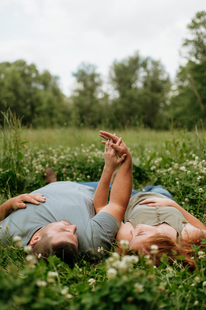 Couple laying in a field of wildflowers for their outdoor summer engagement photos in Indiana