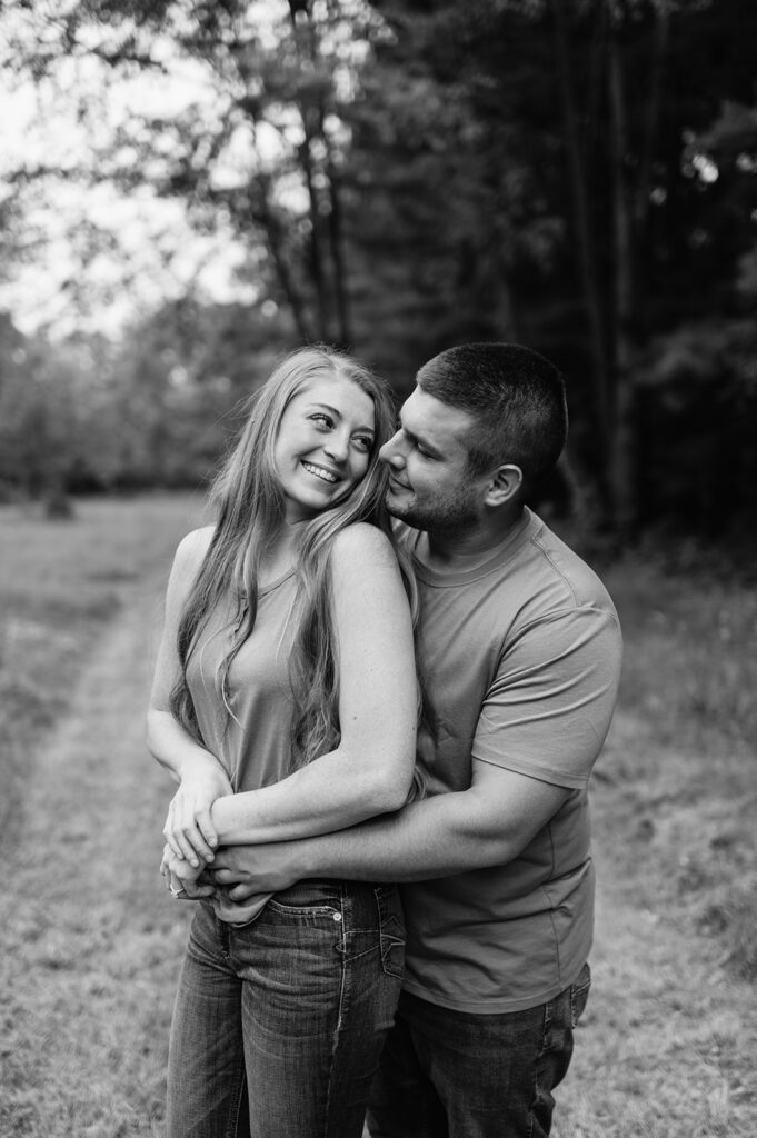 Black and white photo of a man hugging his fiancé from behind