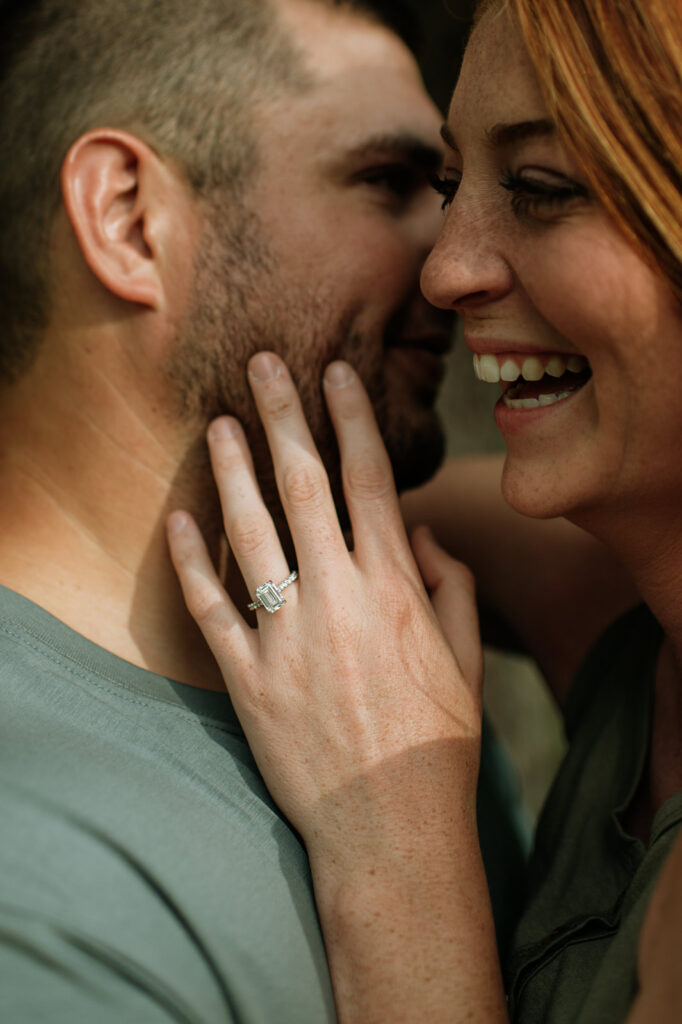 Woman laughing and holding onto her fiancés face while showing off her engagement ring