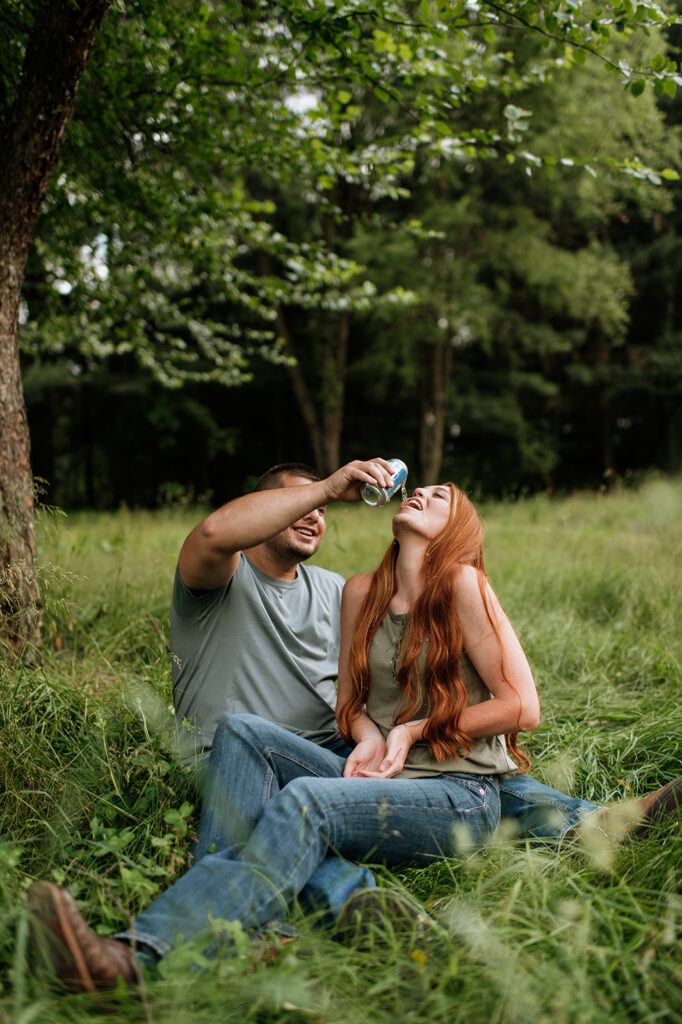 Man spilling Busch Lite into his fiancés mouth during their outdoor summer engagement photos in Indiana