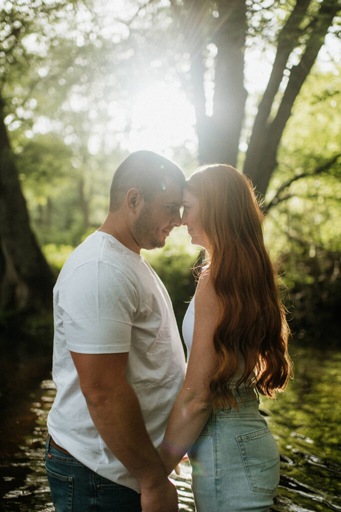 Couples outdoor engagement photos in an Indiana creek with the sun peeking through the trees 