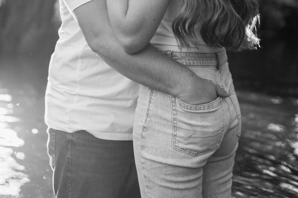 Black and white photo of a man putting his hand in his fiancés back jean pocket 