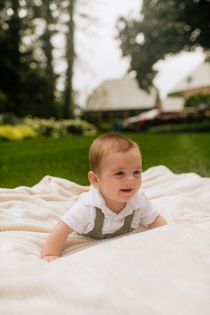 Baby laying on a blanket in the grass during his Lake Michigan family photos at a family lake home in Holland