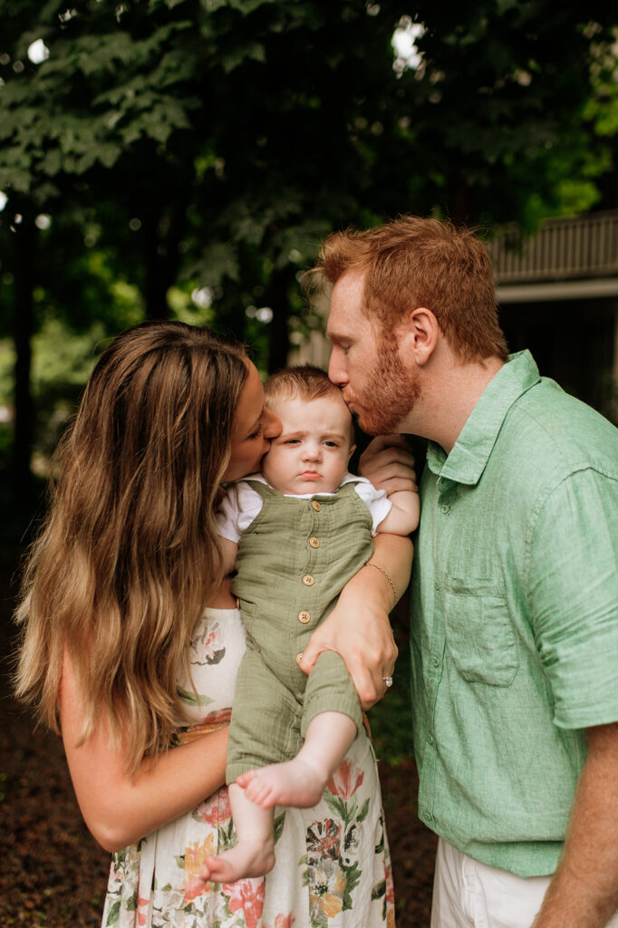 Mother and father kissing their baby on the head during their Lake Michigan family photos at their family lake home in Holland