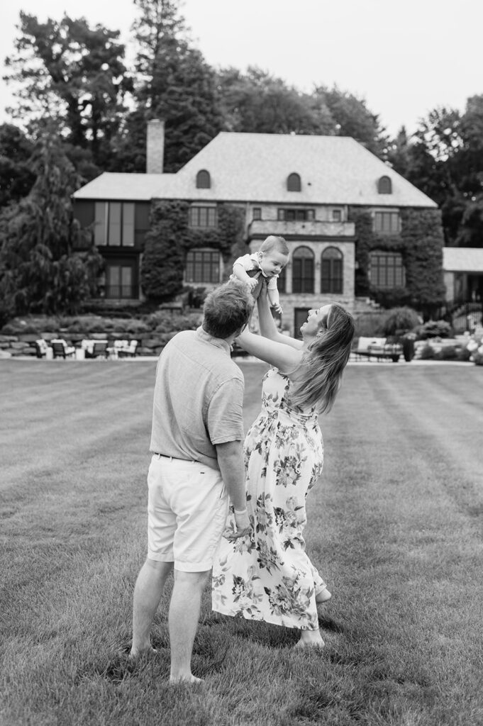 Black and white photo of a mother throwing her baby up in the air playfully during their Lake Michigan family photos at their lake home in Holland