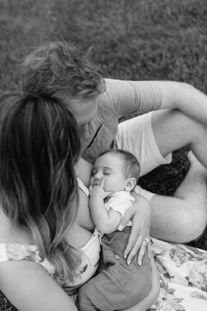 Black and white photo of a man and woman sitting together with their newborn baby during their Lake Michigan family photos in Holland