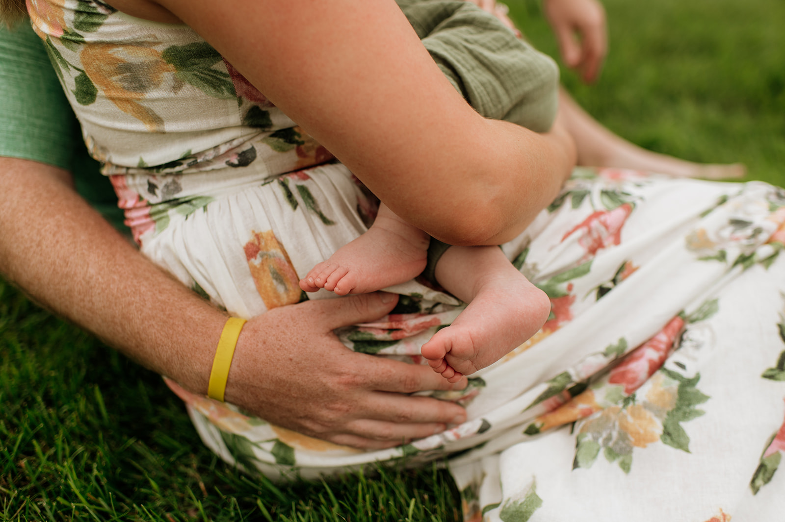 A mother and father holding their newborn baby while they sit in the grass