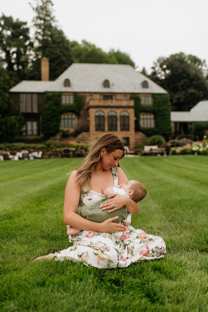 A mother sitting in the grass and holding her baby while he naps during their family session