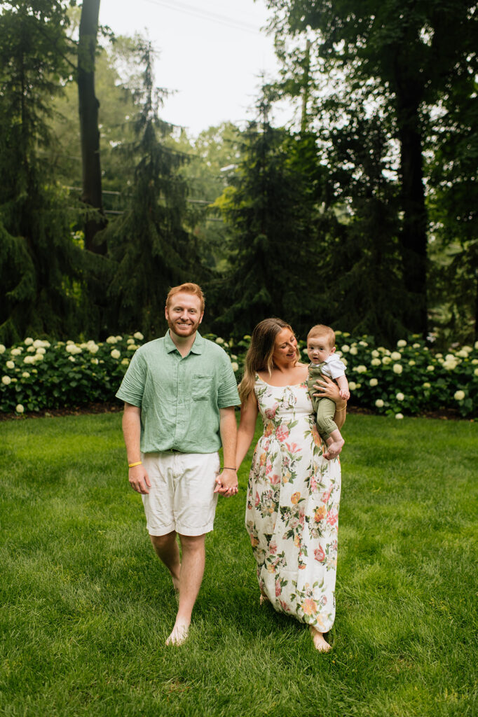 Mother and father holding hands and walking in the grass with their baby for their Michigan family photos