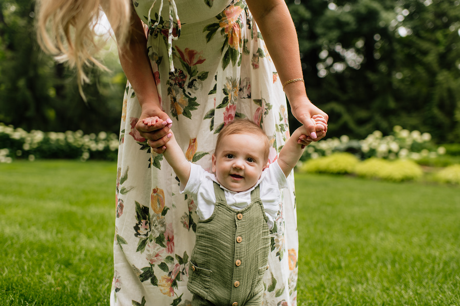 Mother holding her babys hands and helping him walk in the grass