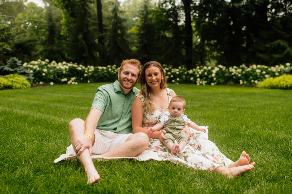 Mother and father sitting in the grass with their baby during their Lake Michigan family photos at their lake home in Holland