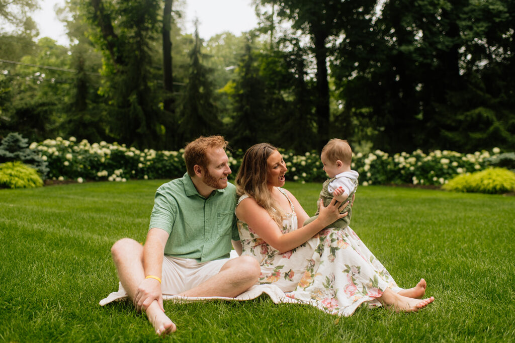 Mother and father sitting in the grass with their baby during their Lake Michigan family photos at their lake home in Holland