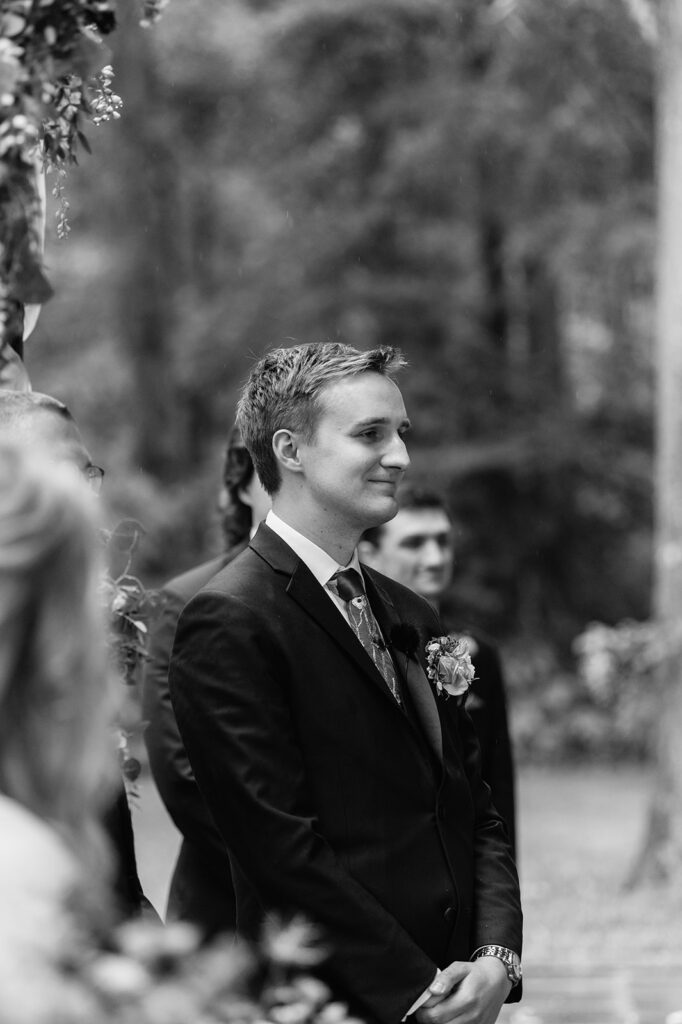 Black and white photo of a groom watching his bride walk down the aisle