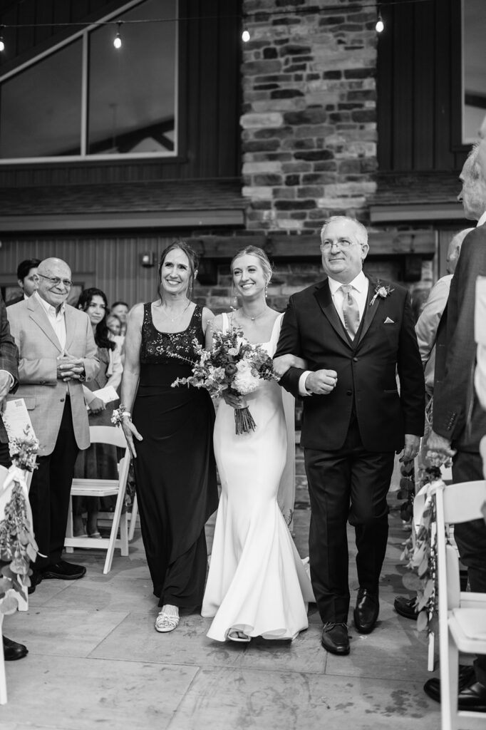 Black and white photo of a bride being walked down the aisle by her parents