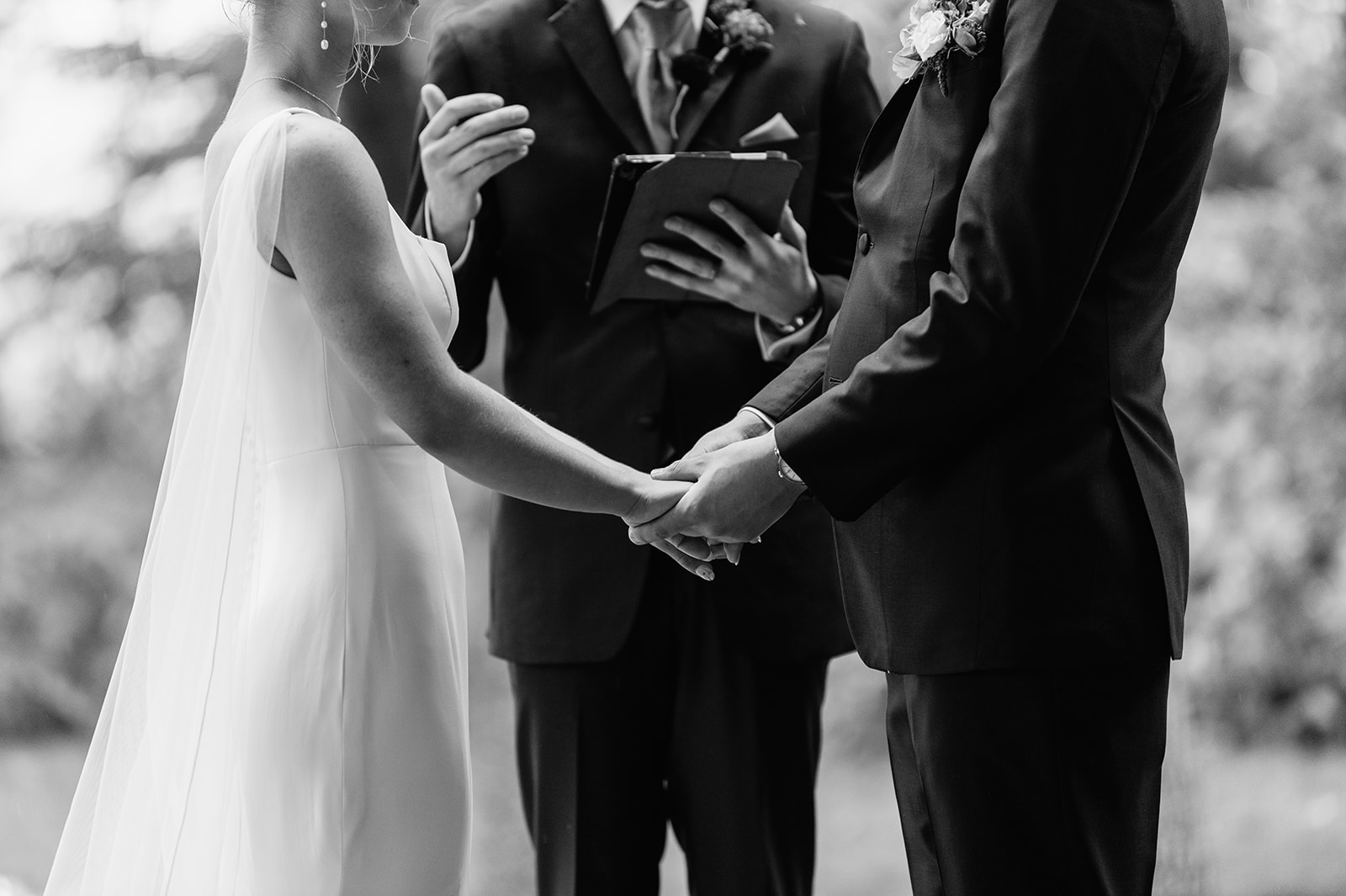 Black and white photo of a bride and groom holding hands during their ceremony