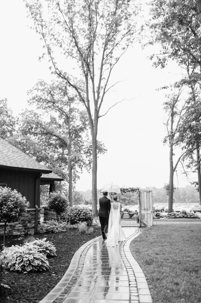 Black and white photo of a bride and groom walking down a path at The Wooded Knot wedding venue on a rainy summer day