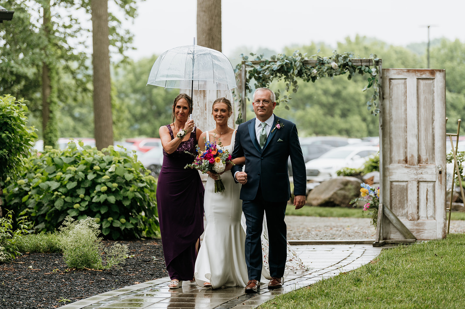 Bride being walked down the aisle by her parents during a rainy wedding ceremony