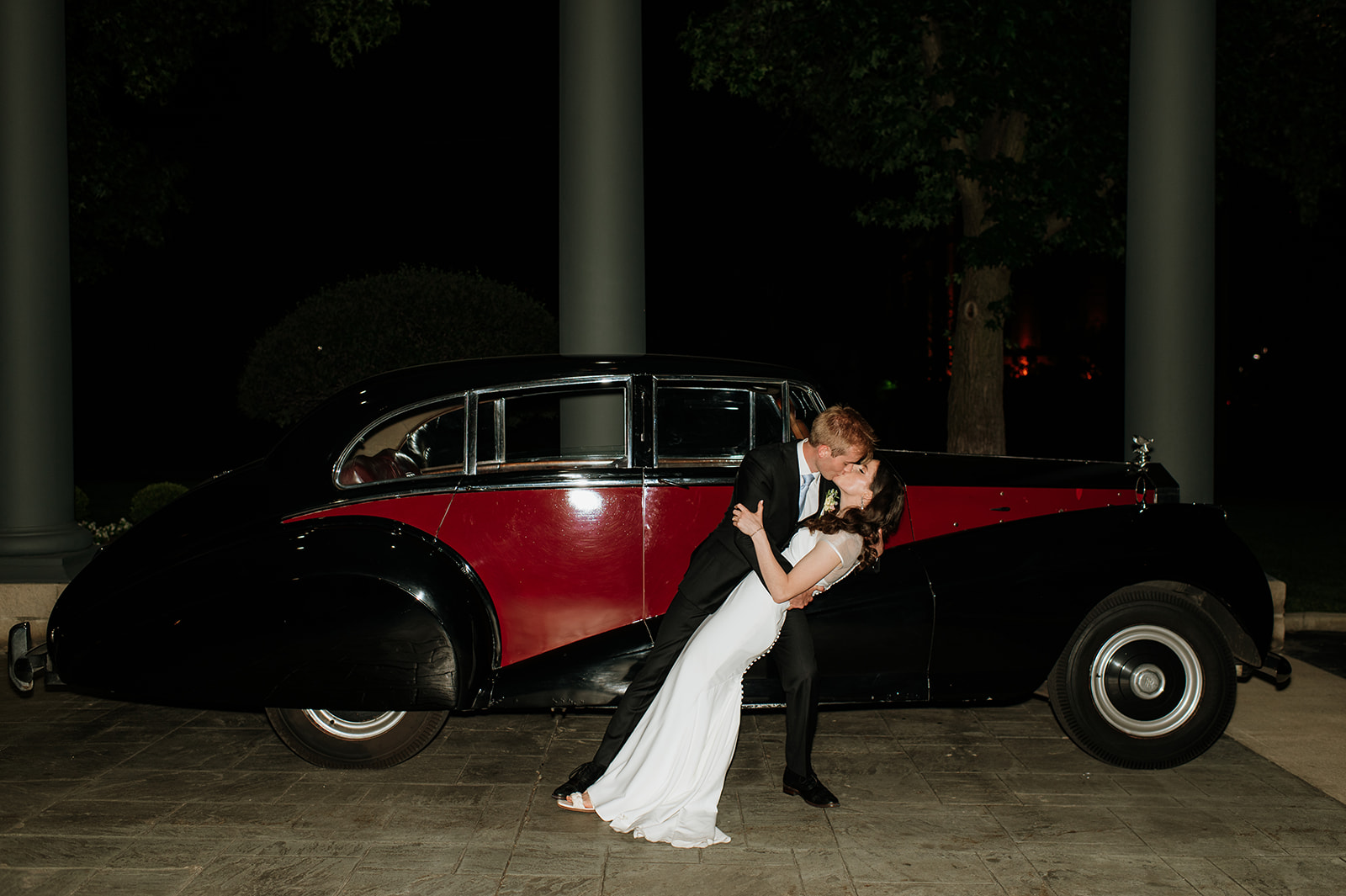 Bride and groom kissing in front of a black and red vintage car during their Ritz Charles Carmel, Indiana wedding