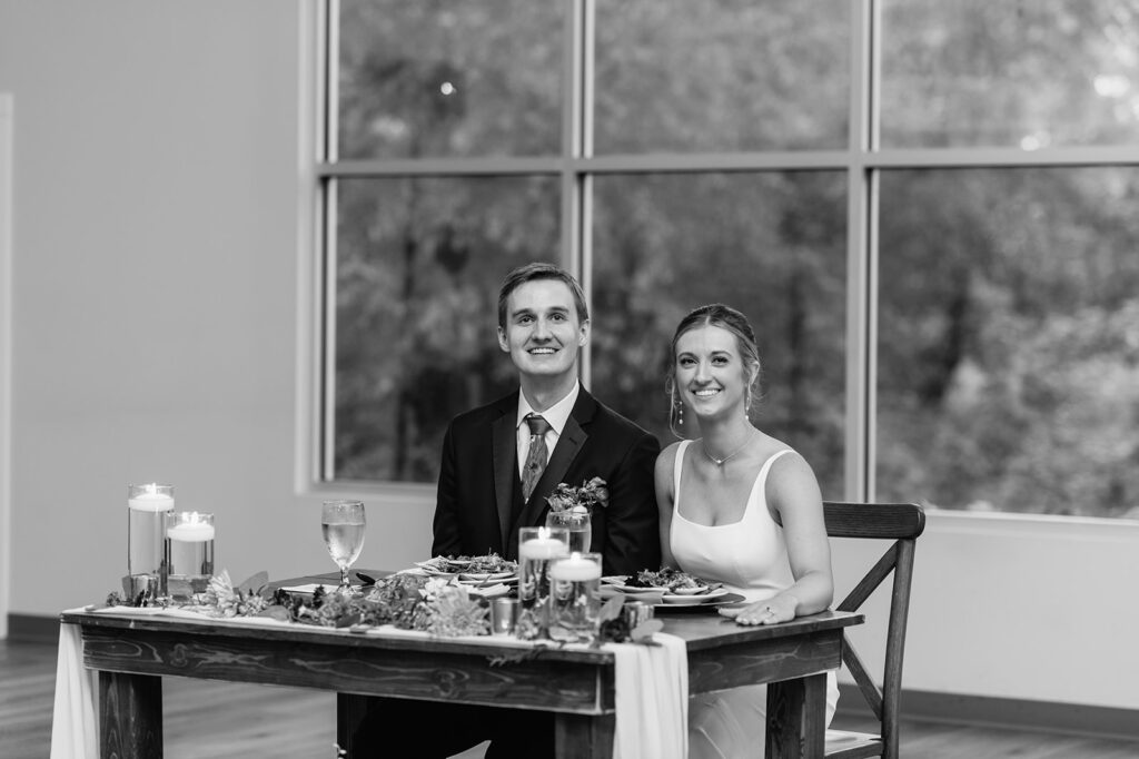 Black and white photo of a bride and groom sitting at their sweethearts table