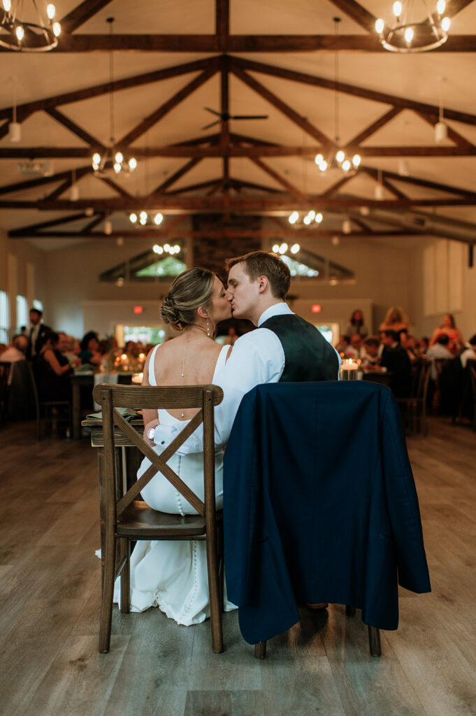 Bride and groom kissing as they sit at their table during their reception