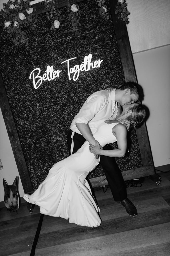 Black and white flash photo of a bride and groom kissing at the end of the night