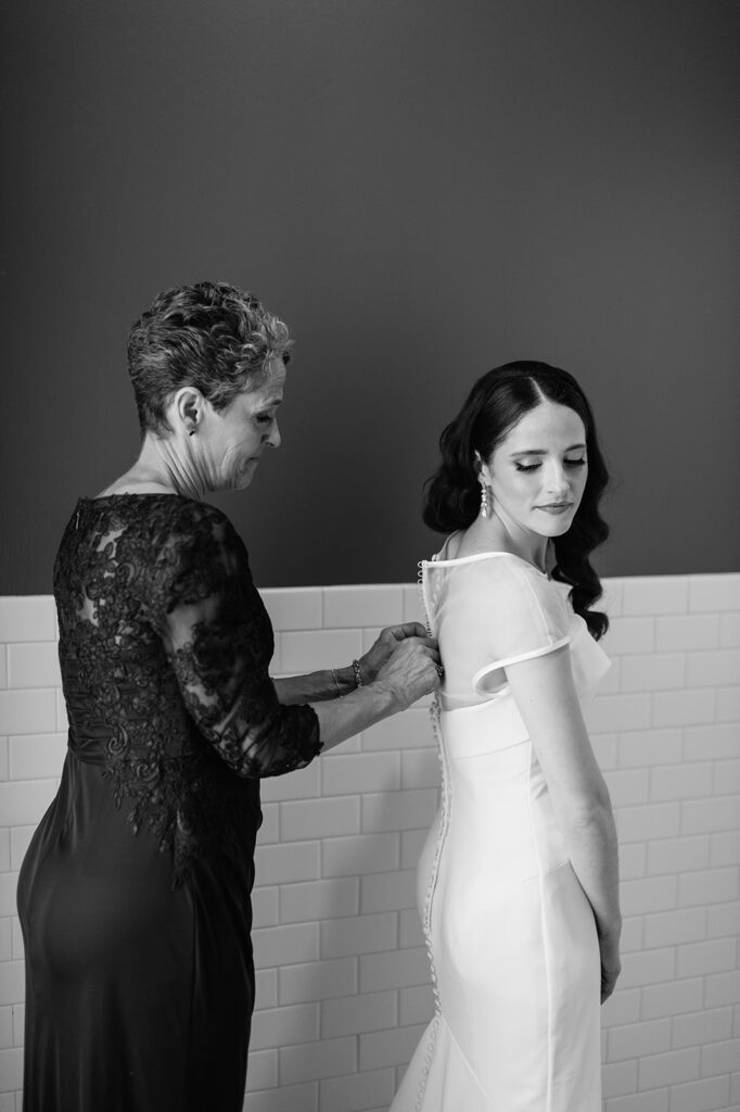 Black and white photo of a bride getting her dress buttoned up