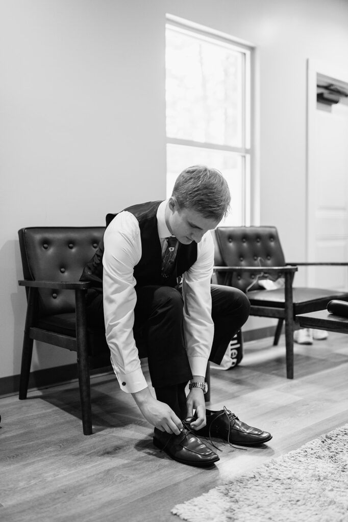 Black and white photo of a groom putting on his shoes