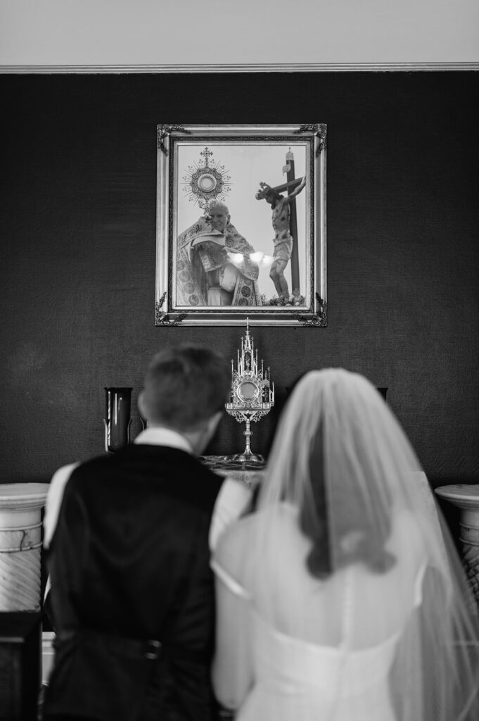 Black and white photo of a bride and groom praying before their St. John the Evangelist Catholic Church wedding ceremony in Indianapolis, Indiana