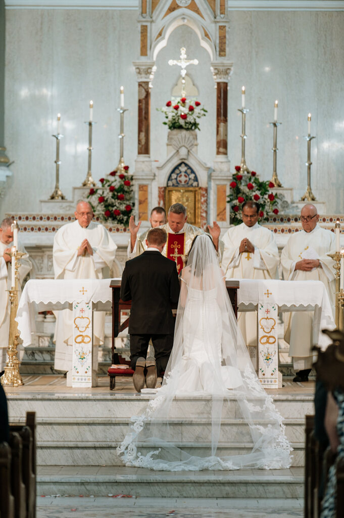 Bride and groom kneeling during their St. John the Evangelist Catholic Church wedding ceremony in Indianapolis, Indiana